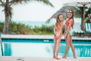 Adorable little girls having fun in outdoor swimming pool on summer vacation photo