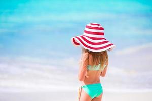 Adorable little girl in big red hat walking along white sand Caribbean beach photo