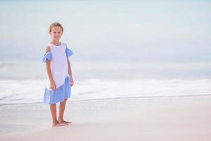 Beautiful little girl in dress at beach having fun. Happy girl enjoy summer vacation background the blue sky and turquoise water in the sea on caribbean island photo