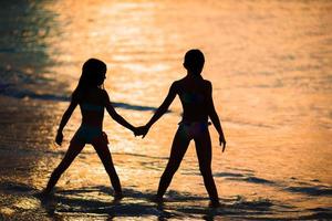 niñas adorables en la playa con una hermosa puesta de sol colorida foto