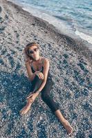 Outdoor fashion portrait of stylish girl wearing trendy sunglasses and jeans jacket on the beach. Hands up, retro filter, flecks of sunlight photo