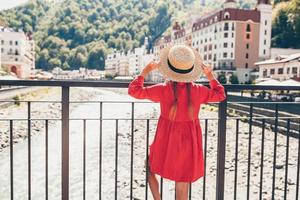 Little girl at hat on the embankment of a mountain river in a European city. photo