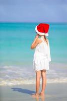 Adorable little girl in Santa hat on tropical beach photo