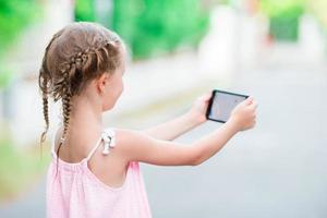 adorable niña con teléfono durante las vacaciones de verano al aire libre foto