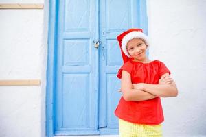 niña pequeña con sombrero de santa al aire libre en la ciudad en vacaciones de navidad foto