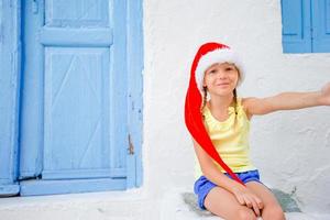 Little girl in santa hat outdoors in the city on Christmas vacation photo