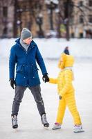 el padre joven y la niña adorable se divierten en la pista de patinaje al aire libre foto