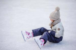 Little adorable girl sitting on ice with skates after fall photo