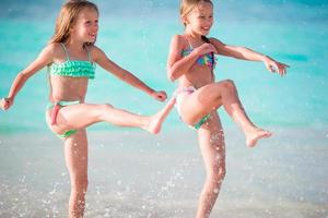 Two little happy girls have a lot of fun at tropical beach playing together at shallow water. Kids splashing. photo