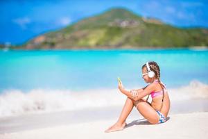 Little girl listening to music on headphones on caribbean beach photo