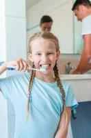 Little adorable girl brushes teeth in the bathroom whilr father brushing teeth too photo