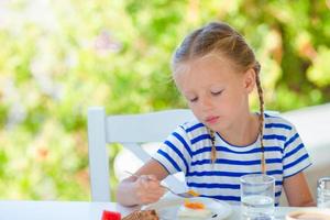 Adorable little girl having breakfast at outdoor cafe early in the morning photo