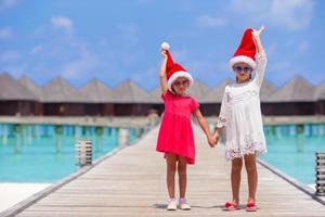 niñas adorables con sombreros de santa durante las vacaciones en la playa en el embarcadero de madera foto