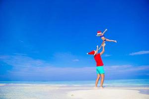 padre feliz y su adorable hijita con sombrero de santa en la playa tropical foto