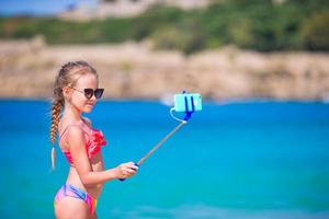 Little girl taking selfportrait by her smartphone on the beach. Kid enjoying her suumer vacation and making photos for memory