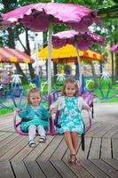Two little fashion lovely sisters ride on the carousel in the park photo