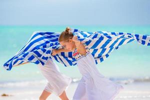 niñas divirtiéndose corriendo con toallas en una playa tropical con arena blanca y agua turquesa del océano foto