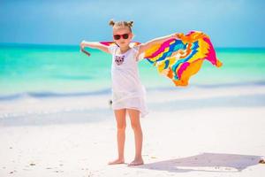 Little girl having fun running with towels on tropical beach photo