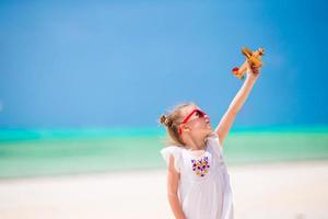 Adorable little girl with toy airplane in hands on white tropical beach