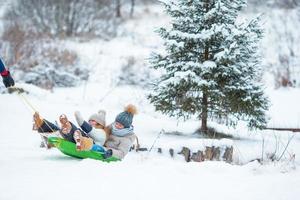 Little girls enjoying sledding in winter day. Father sledding his little adorable daughters. Family vacation on Christmas eve outdoors photo