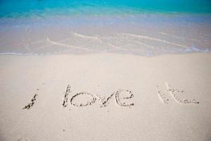 palabra me encanta escrita a mano en una playa de arena con una suave ola oceánica en el fondo foto