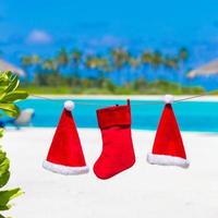 sombreros rojos de santa y calcetín de navidad entre palmeras en playa blanca foto