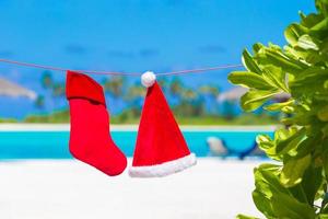 Red Santa hat and Christmas stocking between palm trees on white beach photo