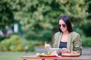 Young woman eating take away noodles on the street photo