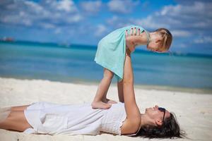 la joven y hermosa madre y su adorable hijita se divierten en la playa tropical foto
