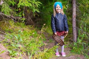 Little happy girl pick up mushrooms in autumn forest photo
