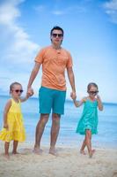 Happy father with his two daughters walking on tropical beach vacation photo