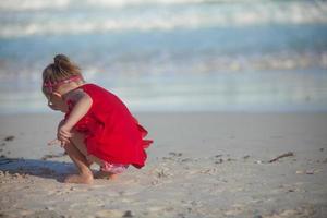 Adorable little girl in red dress playing at tropical beach photo