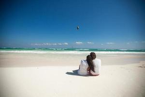 vista trasera de una pareja joven sentada en una playa blanca tropical foto