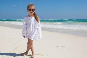 adorable niña pequeña con vestido blanco caminando en una playa exótica foto