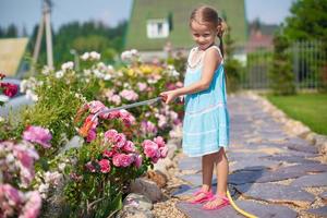 linda chica con vestido azul regando flores con una manguera en su jardín foto