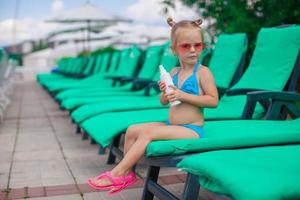 Little girl sitting on the rug and rubs feet sunscreen photo