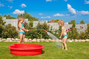 Two little sisters frolicing, splashing and having fun in their yard photo