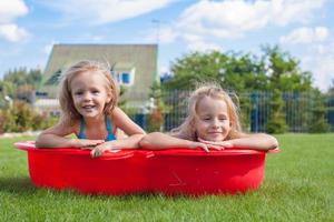 Two little sisters frolicing and splashing in their yard in small pool photo