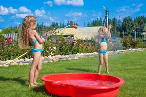 Two little sisters frolicing, splashing and having fun in their yard photo