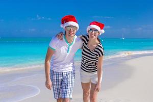 joven pareja feliz en sombreros rojos de santa en playa tropical foto