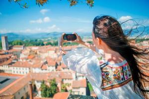 Young caucasian woman making photo of european old city by mobile phone from the observation place