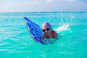 Little girl swimming on surfboard in the turquoise sea photo
