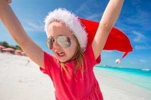 Little adorable girl in red Santa hat have fun on the beach photo