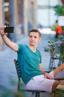 turista caucásico con smartphone tomando selfie sentado en un café al aire libre. foto