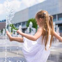 Little girl have fun in open street fountain at hot summer day photo