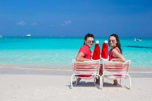 Happy young couple with red Santa Hats sitting on beach chairs photo