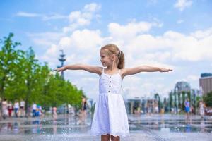 Little girl have fun in open street fountain at hot summer day photo