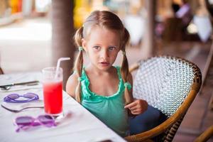 Adorable little girl having breakfast and drinking fruit cocktail photo