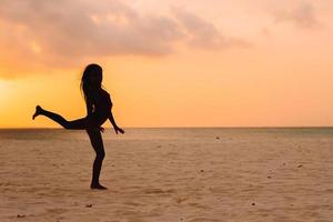 Adorable happy little girl on white beach at sunset. photo