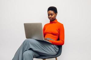 mujer negra con una camisa roja en un fondo blanco usando una computadora portátil foto